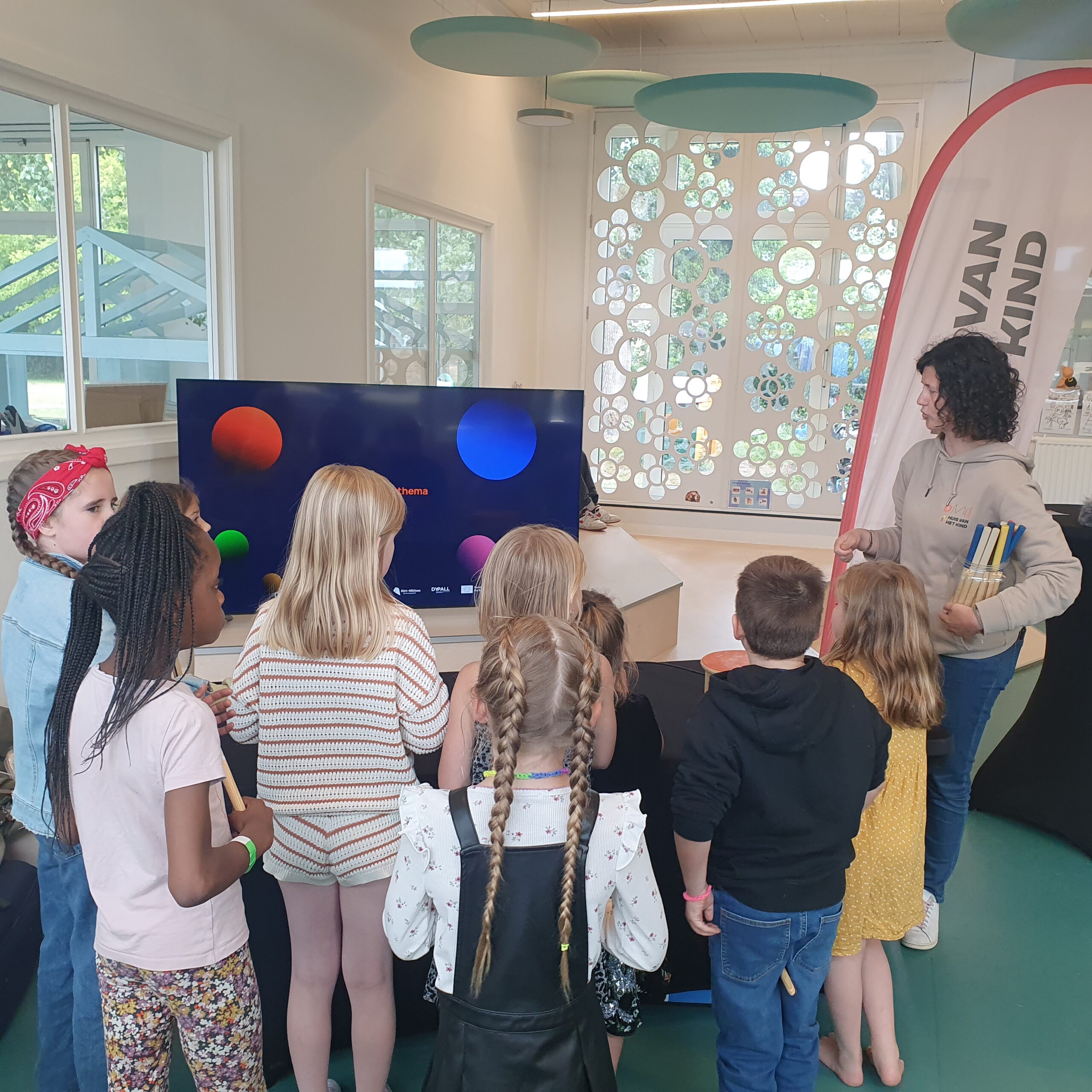 Kinderen nemen deel aan een interactieve bevraging met een begeleider en digitaal scherm.